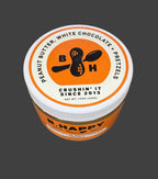 Jar of B. Happy peanut butter with white chocolate and pretzels on a wooden surface