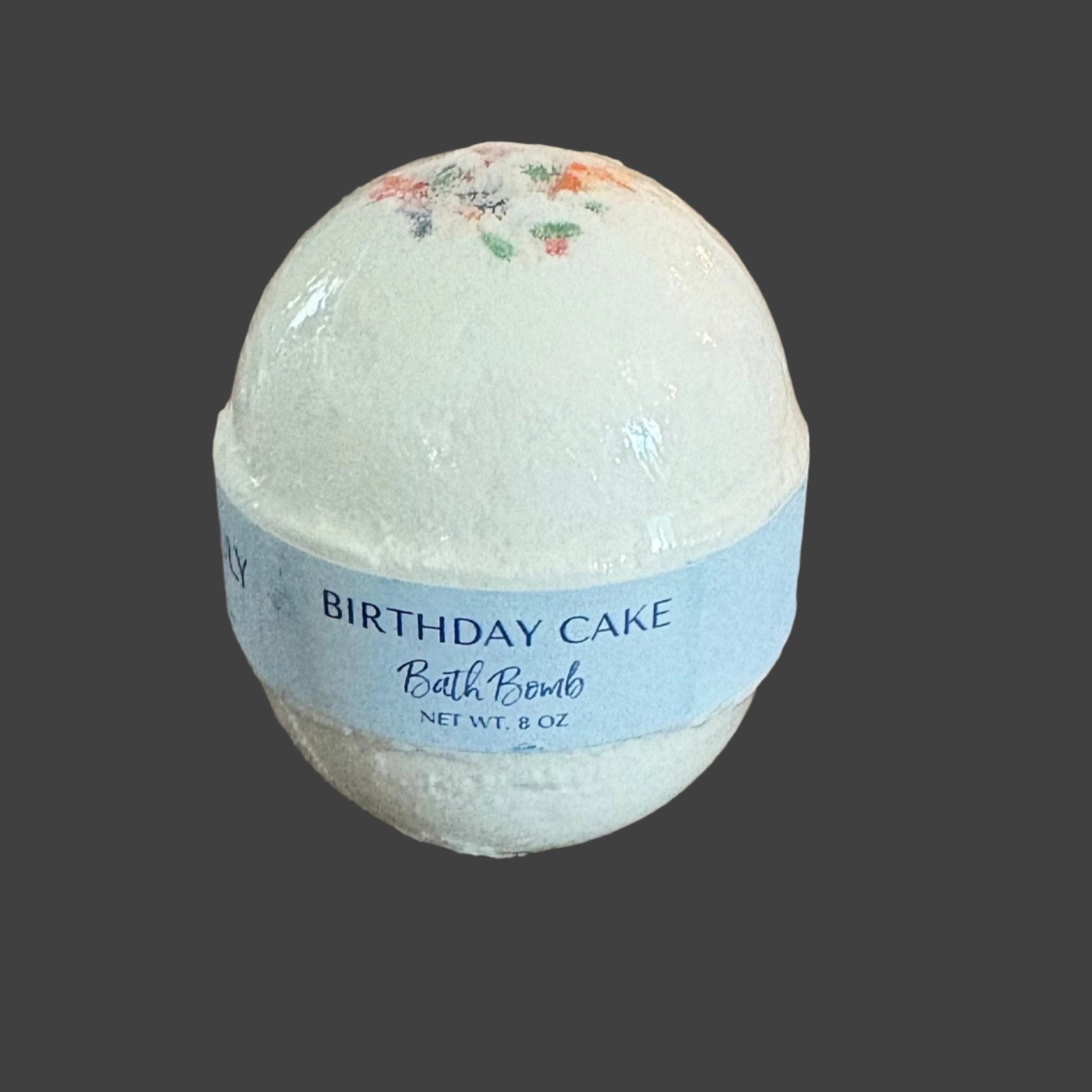 Bath bomb labeled 'Birthday Cake' on a wooden surface