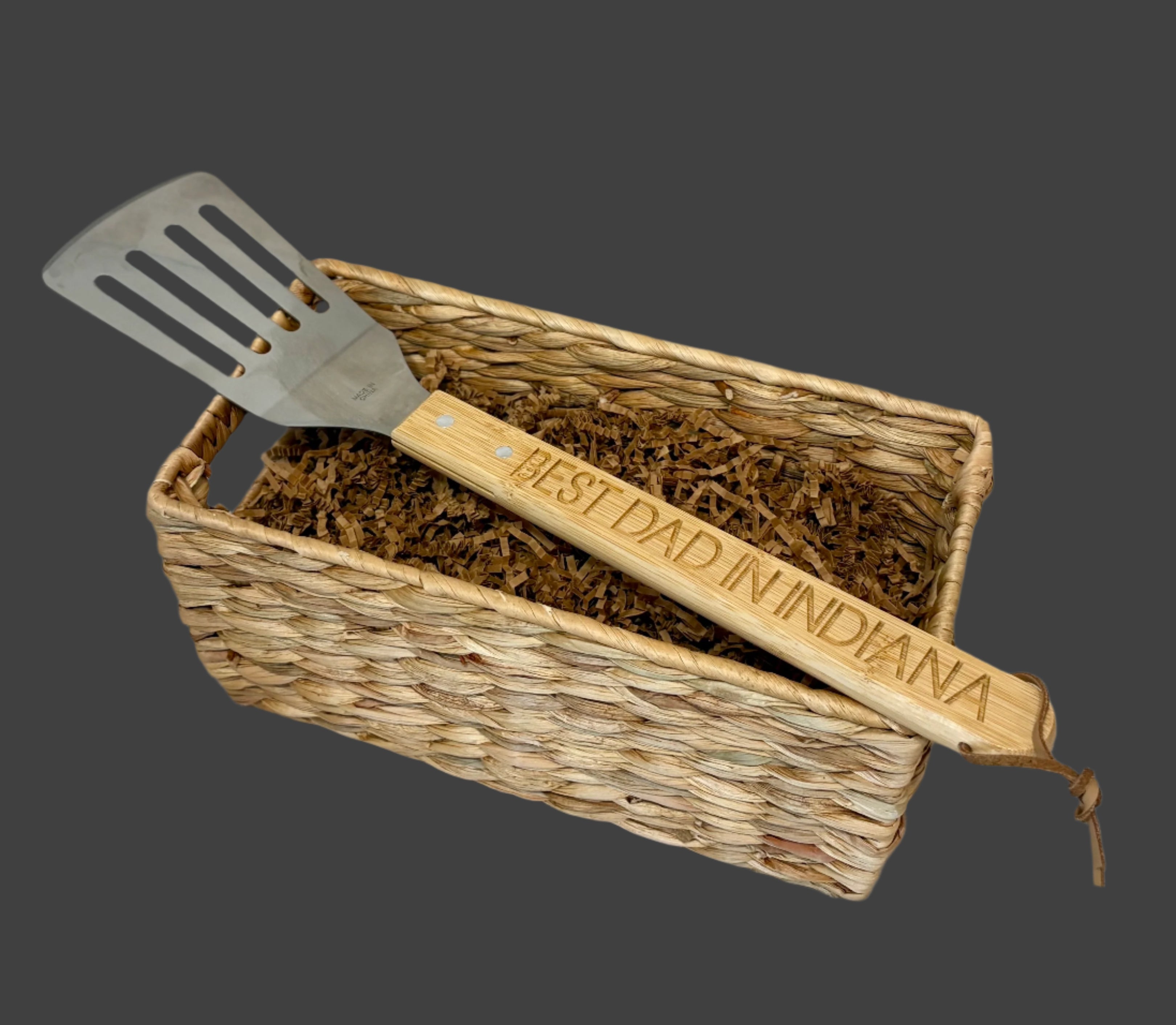 Spatula with 'Best Dad in Indiana' engraving in a woven basket on a light background