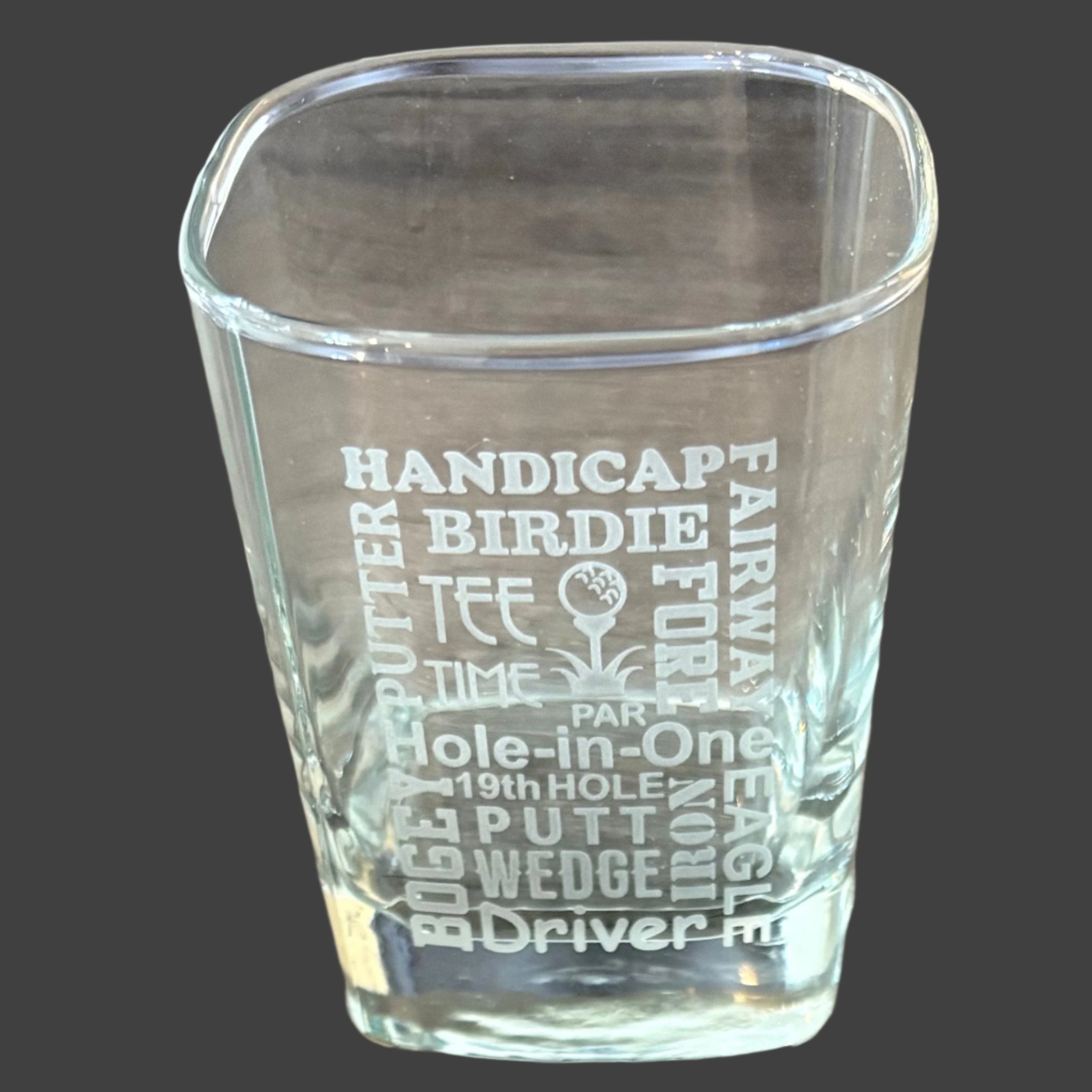 Clear glass with engraved golf-themed text on a wooden surface