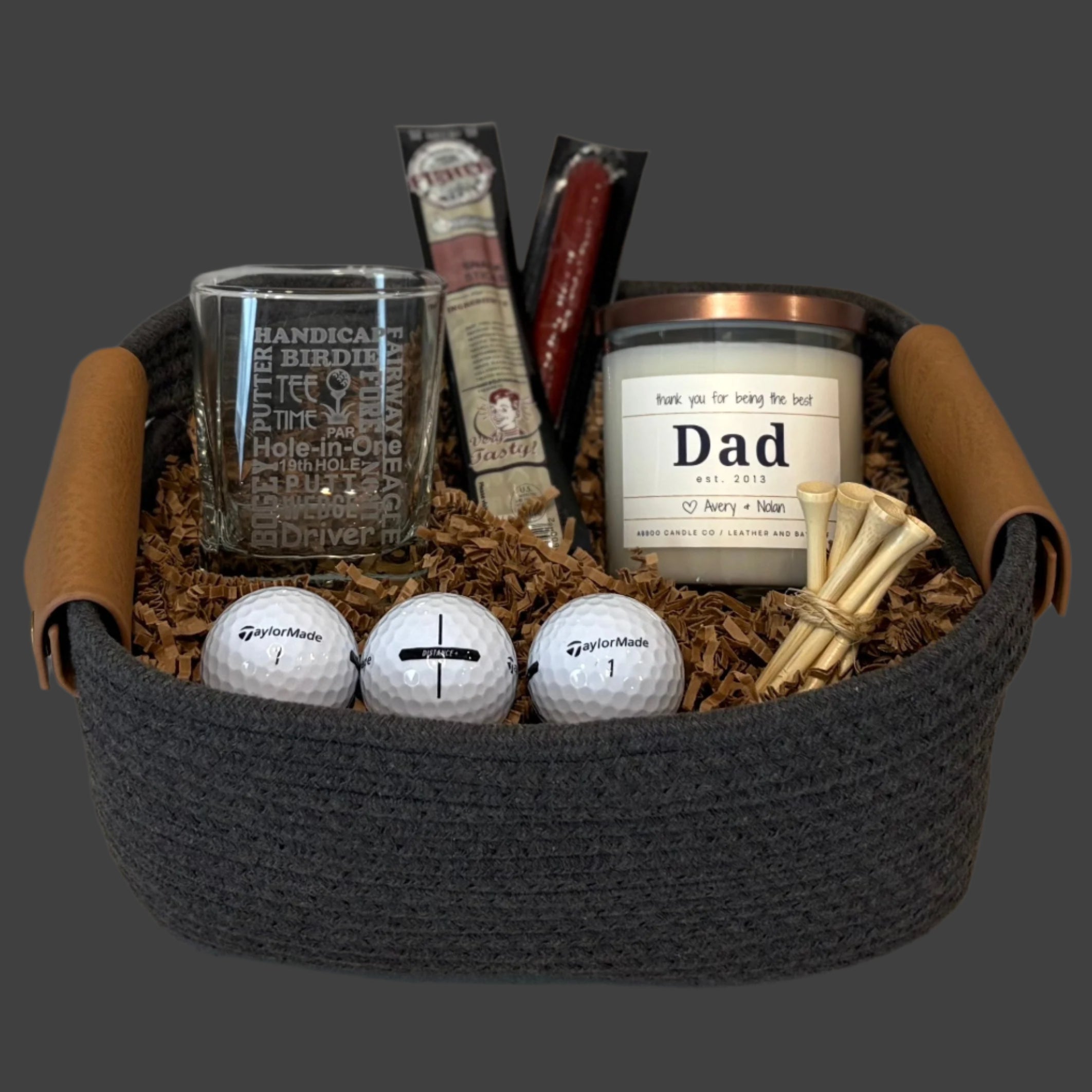 Golf themed gift basket with a golf glass, a personalized candle, and other golf items on a wooden surface.