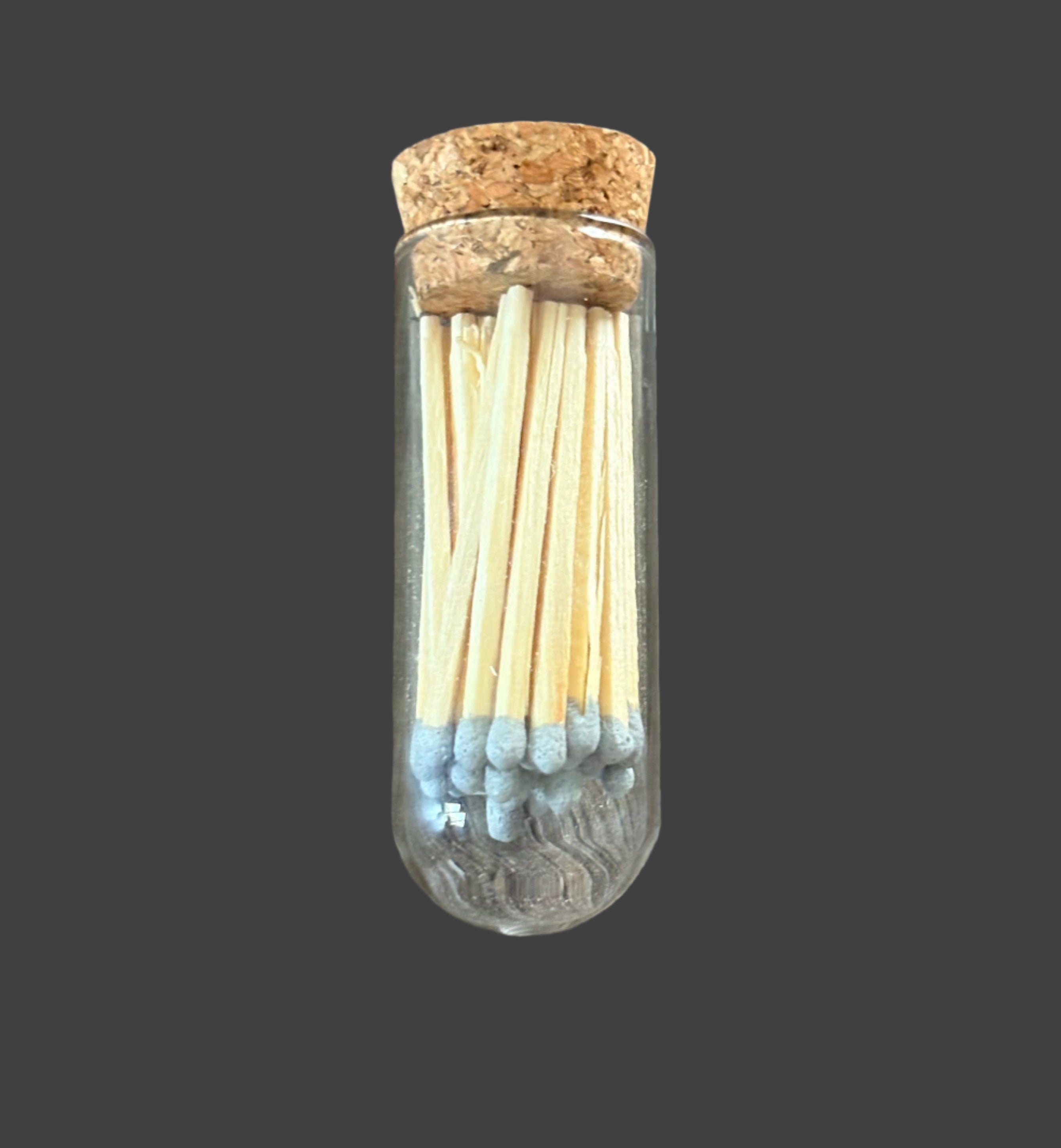 Clear glass tube with cork lid containing matches on a wooden surface