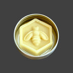 Beeswax lotion bar with bee design in a metal container on a wooden surface
