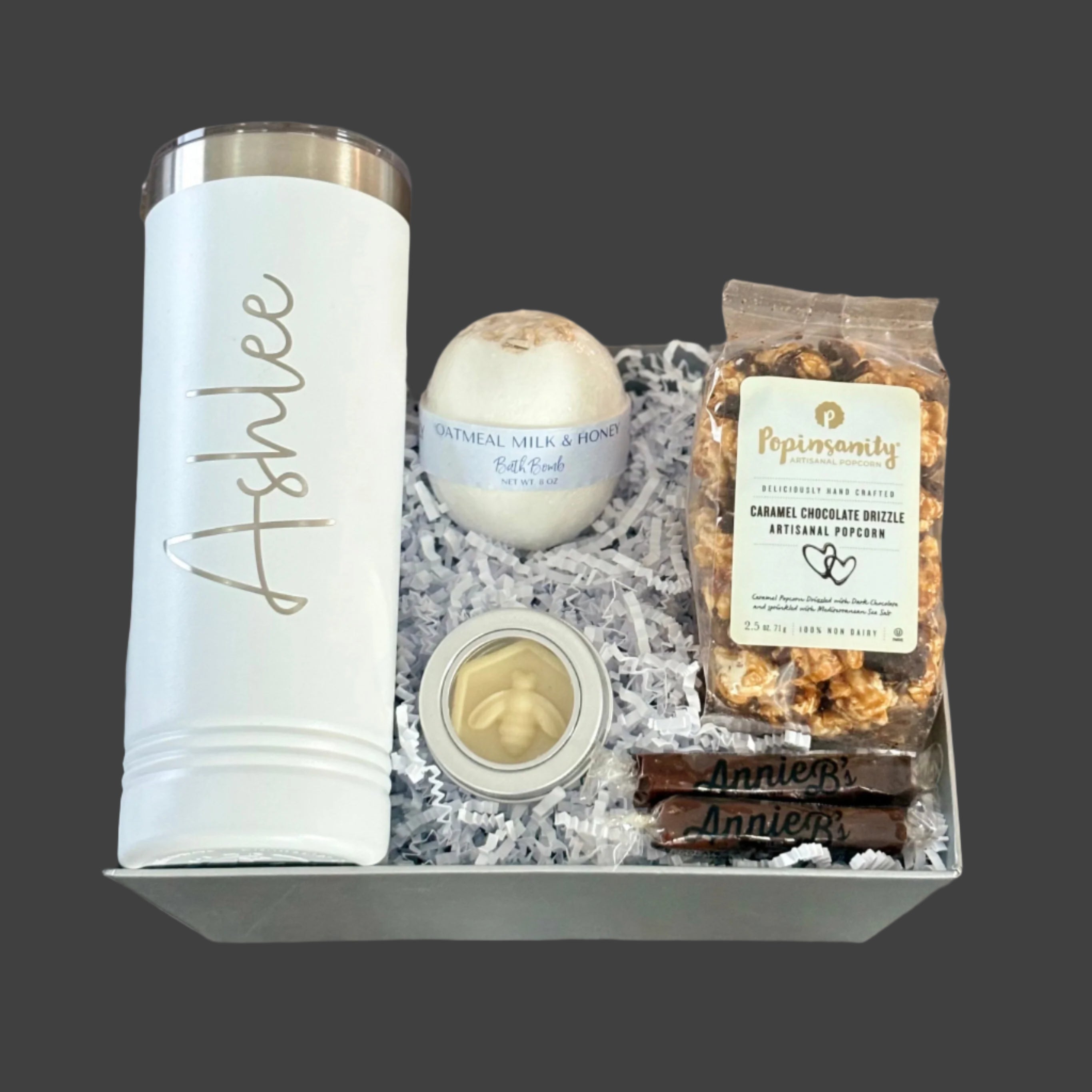 Gift box with personalized tumbler, bath bombs, and snacks on a wooden surface